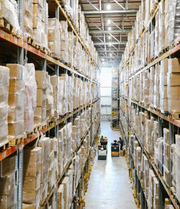 Long warehouse aisle lined with tall racking of shrink-wrapped pallets