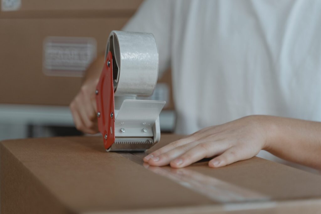 Hands sealing a cardboard box with a packing-tape gun