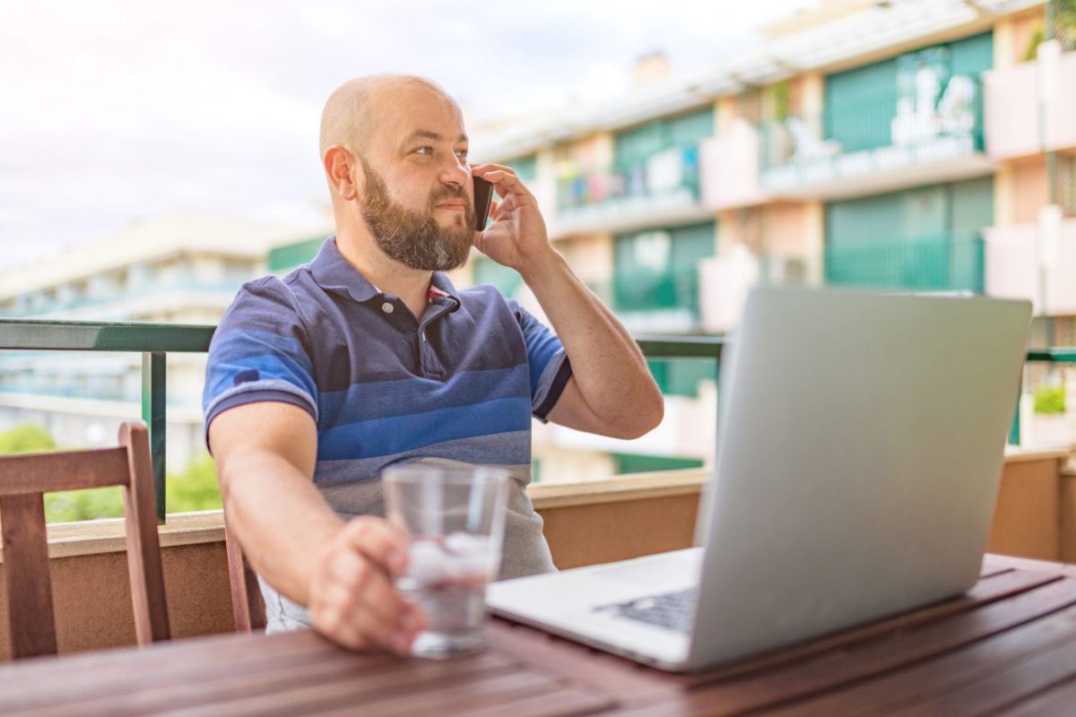 Man working outdoors on a phone call beside a laptop