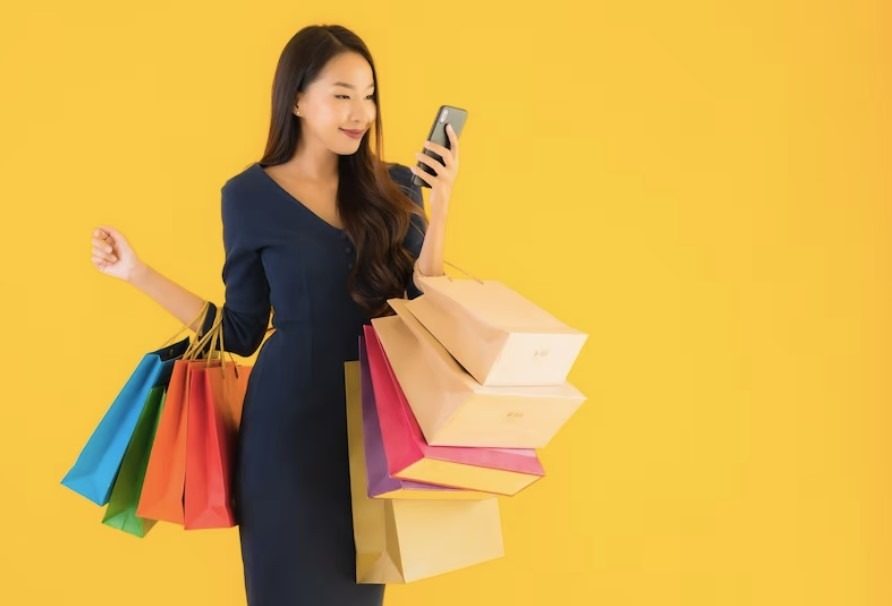 Woman holding shopping bags and a phone against a yellow background